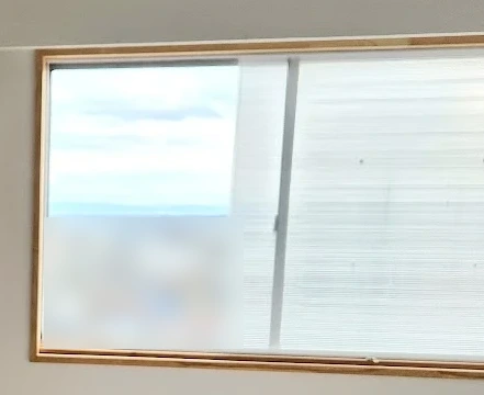 寝室の内窓の左側を開けたところ。開けた側は空と海が見えて、閉めた側はぼやけています(建物はぼかしています)
